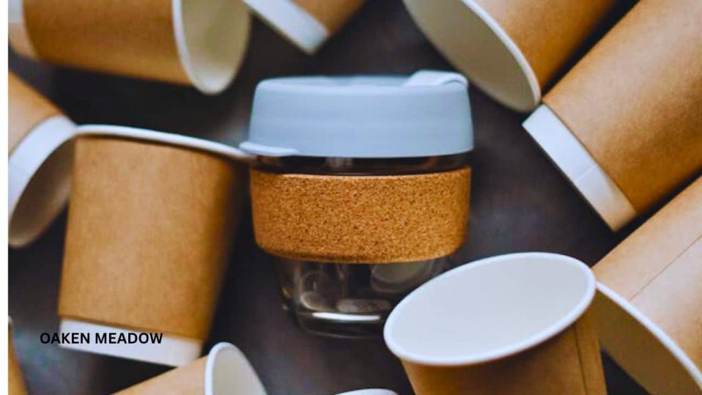 A collection of sustainable lifestyle products including bamboo cutlery, a glass water bottle, and a compostable plant-based food container on a wooden table.